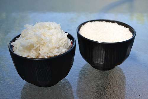 Una taza de arroz cocido y una taza de arroz crudo.