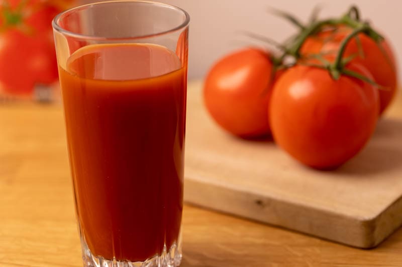 Vaso de jugo de tomate y tomates en el fondo