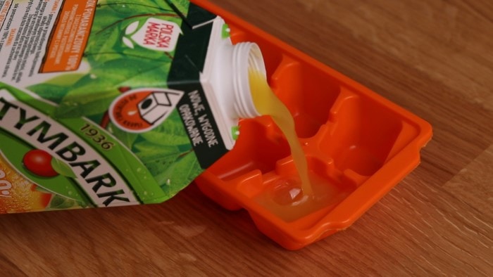Verter jugo de naranja en una bandeja de cubitos de hielo