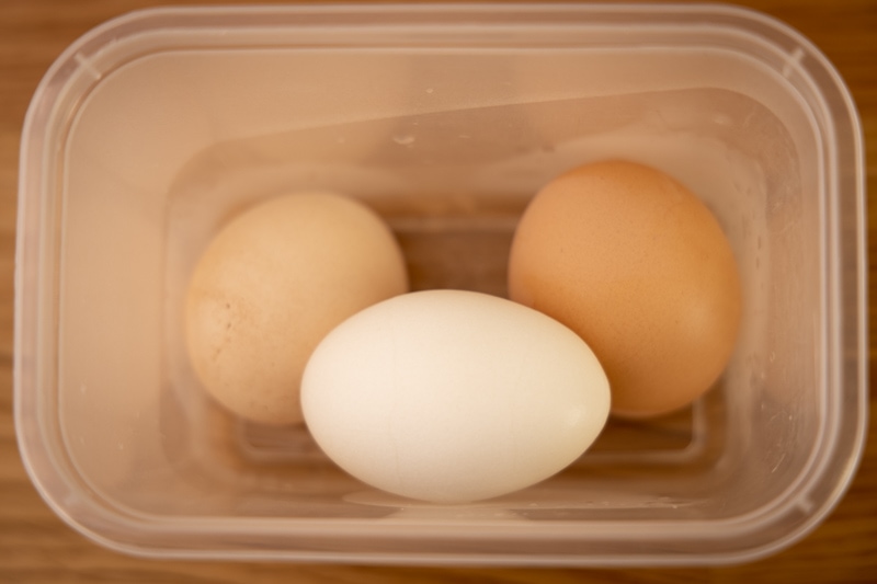 Huevos cocidos duros sin pelar en recipiente de plástico