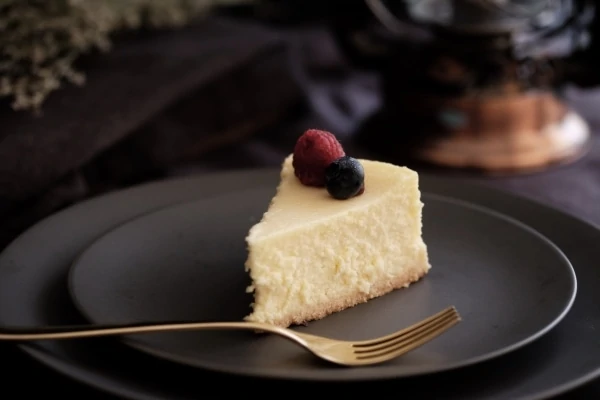Cheesecake slice garnished with fruit on a black plate